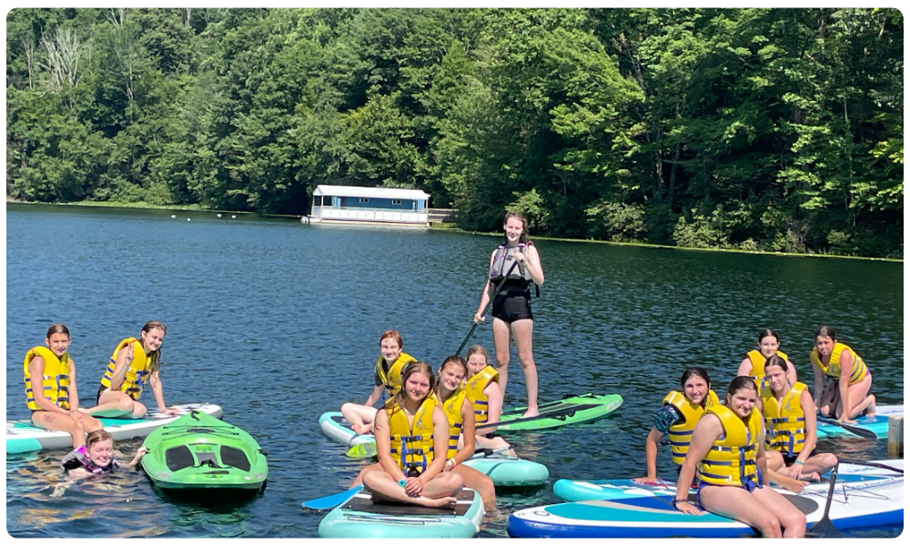older girls sitting on paddle boards at Camp Archbald 